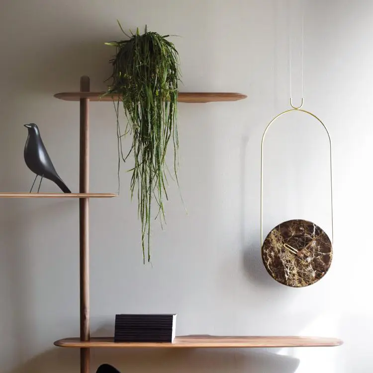The Nomon Colgante clock hangs on a wall next to a plant and a decorative bird.